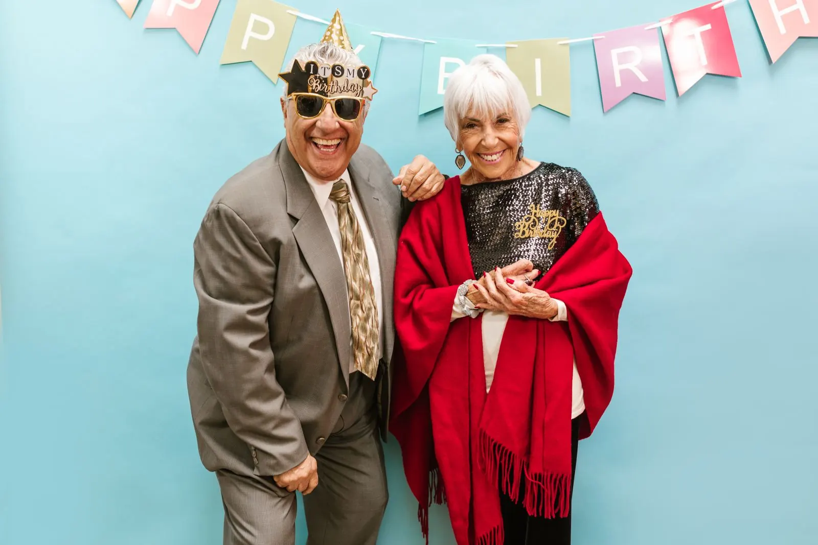 Two guests laughing in party hats in front of a photo booth backdrop