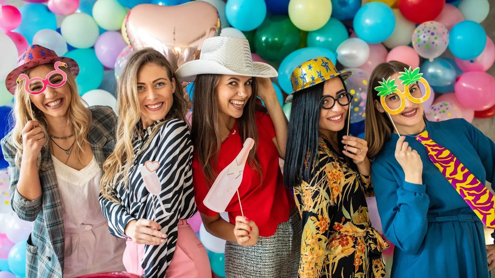 Women holding photo booth props in front of a balloon backdrop